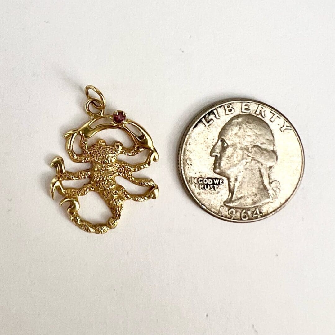Gold scorpion pendant next to a quarter.