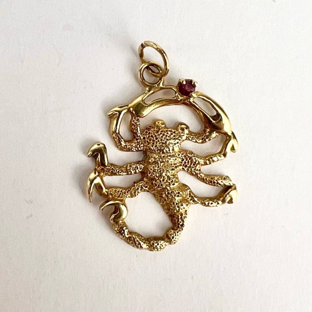 Golden scorpion pendant with small gemstone.