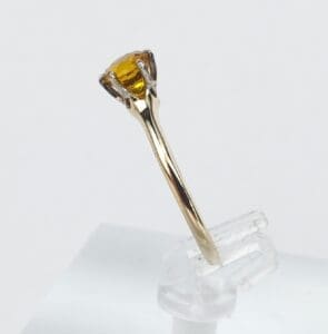 Gold ring with yellow gemstone on stand.