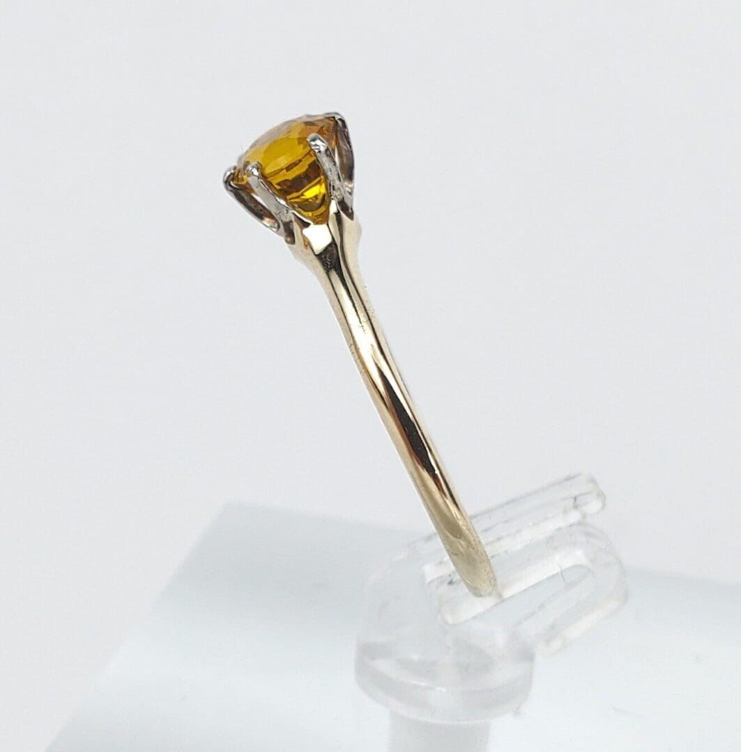 Gold ring with yellow gemstone on stand.