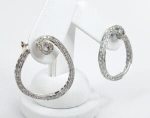 Silver swirl earrings on white stand.