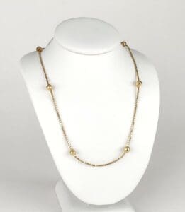 Gold beaded necklace on white display stand.