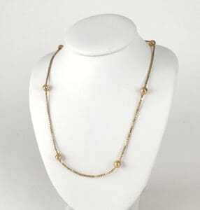 Gold necklace with beads on display stand.