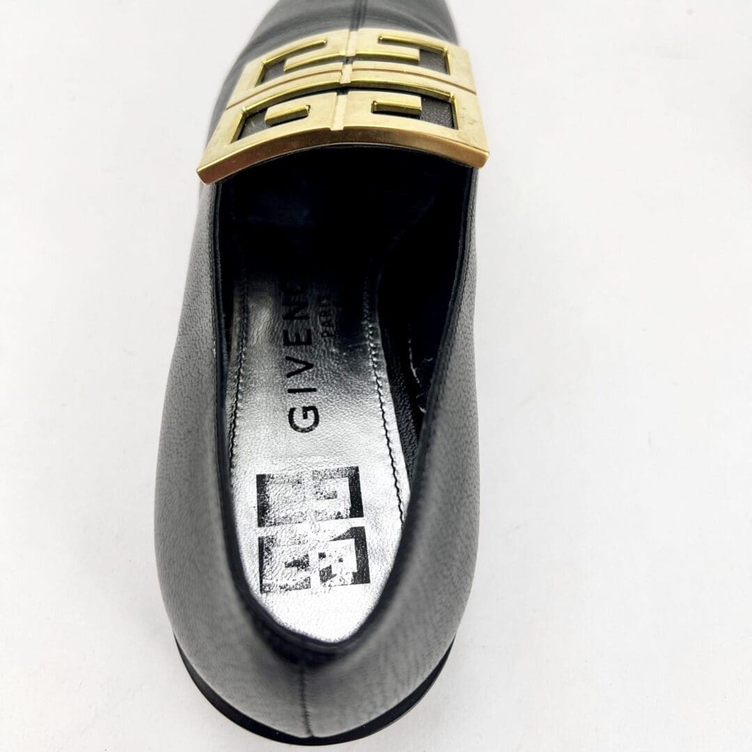 Black shoe with gold buckle design.