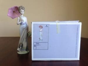 Porcelain figurine with pink umbrella and box.