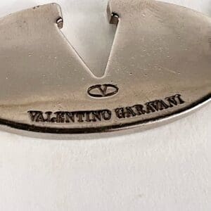 Silver metal tag with Valentino Garavani engraving.