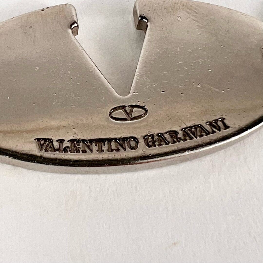 Silver metal tag with Valentino Garavani engraving.