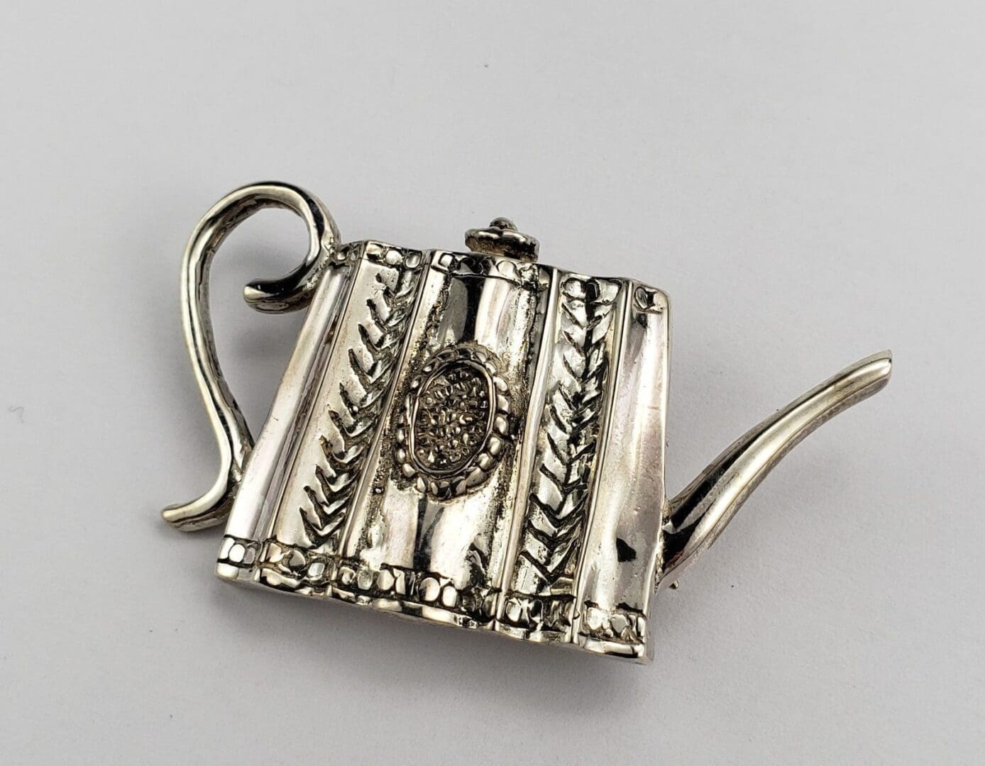 Ornate silver teapot brooch with intricate details.