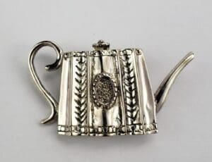 Ornate silver teapot brooch with handle.