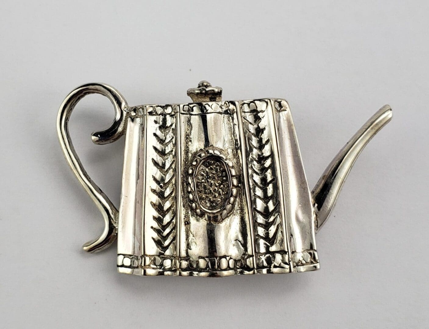 Ornate silver teapot brooch with handle.
