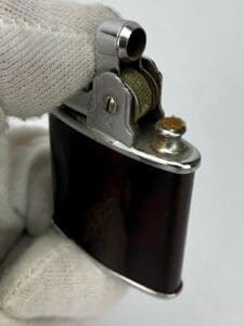 Gloved hand holding vintage metal lighter.