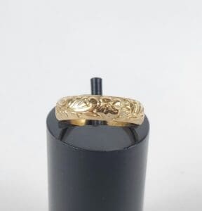 Gold ring with intricate design on stand.