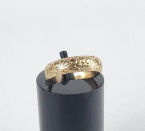 Gold ring with engraved design on stand.