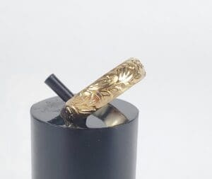 Engraved gold ring on black stand.