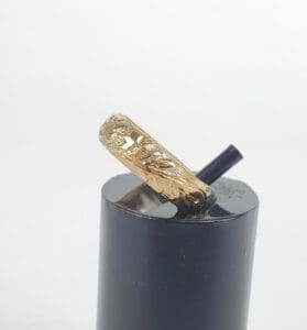 Gold engraved ring on black stand.