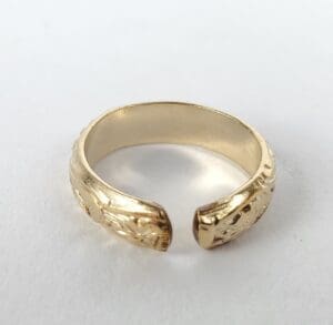Gold open-ended engraved ring on white background.
