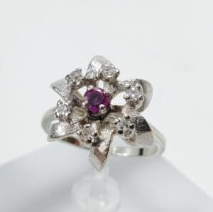 Silver flower ring with central purple gem.