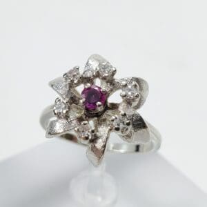 Silver flower ring with central purple gem.