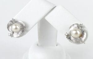 Silver earrings with pearls on display stand.