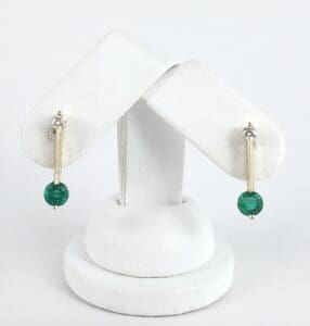 Gold earrings with green gemstone on stand.