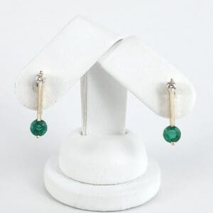 Gold earrings with green gemstone on stand.