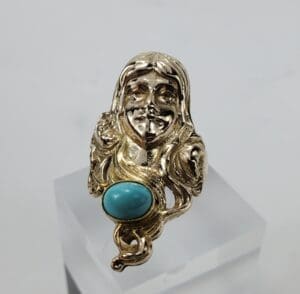 Gold ring with face and turquoise stone.
