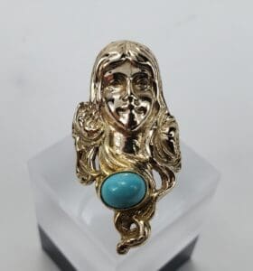 Gold ring with turquoise stone and face.