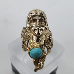 Gold ring with turquoise stone and face.
