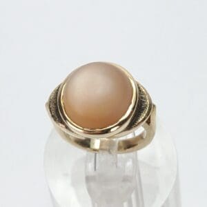 Gold ring with a round beige stone.