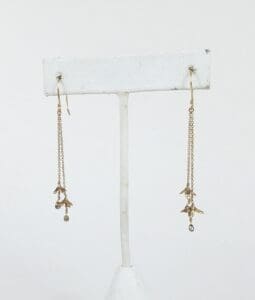 Gold dangling earrings on white display stand.