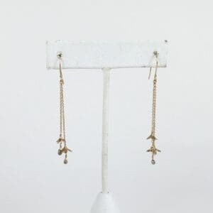 Gold drop earrings on white stand.