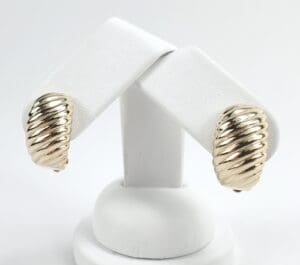 Gold twisted earrings on white display stand.