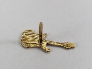 Gold guitar-shaped lapel pin on display.