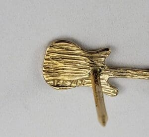 Gold guitar-shaped pin with textured surface.