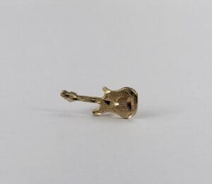 Gold guitar-shaped pin on white background.
