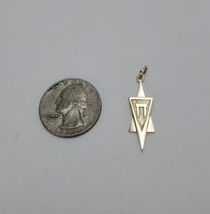 Quarter beside geometric pendant on gray background.