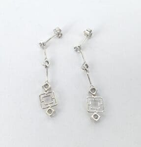 Silver geometric dangle earrings on white background.