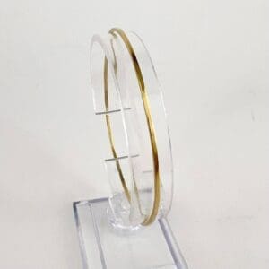 Thin gold bracelet on clear display stand.