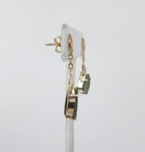 Gold earrings with green gemstone on stand.