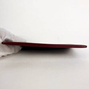 Red leather wallet held by gloved hand.