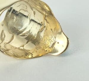 Gold-toned jewelry piece with engraved signature.