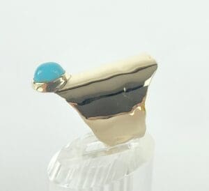 Gold ring with turquoise stone on stand.