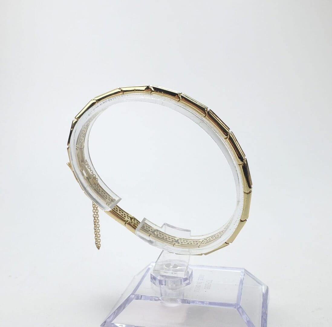 Gold bracelet on a clear stand.