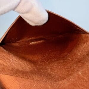 Gloved hand holding open empty brown wallet.