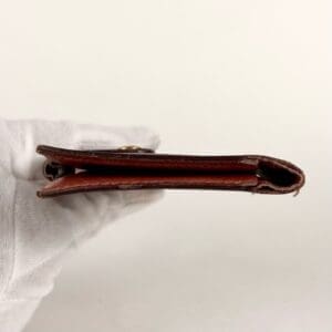 Gloved hand holding thin leather wallet.