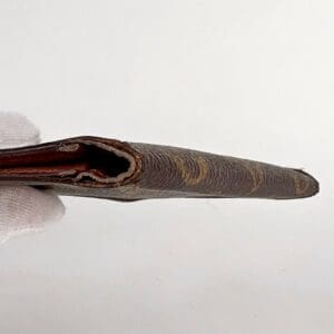 Gloved hand holding thin, brown wallet.