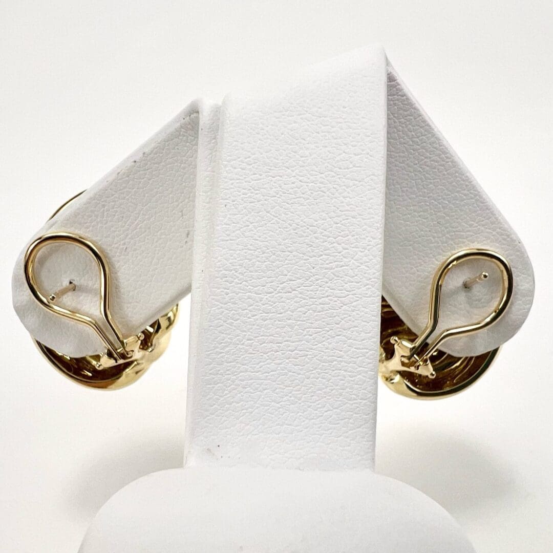 Gold earrings displayed on white stand.