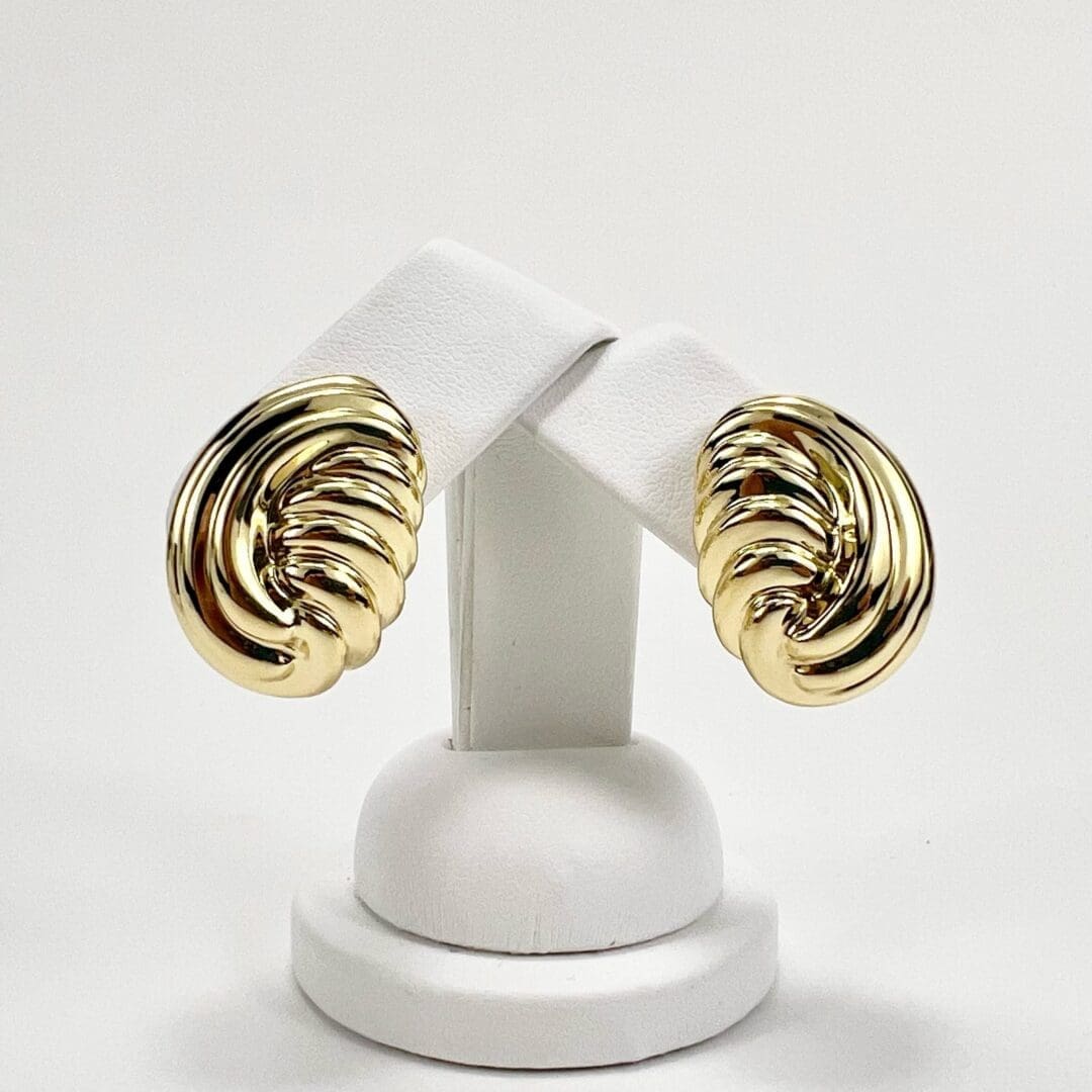 Gold shell-shaped earrings on display stand.