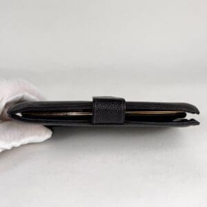 Black leather wallet held by gloved hand.