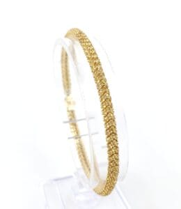 Gold bracelet displayed on a clear stand.